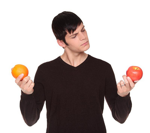 Isolated studio shot of a Caucasian man looking at fruit comparing an apple to an orange.